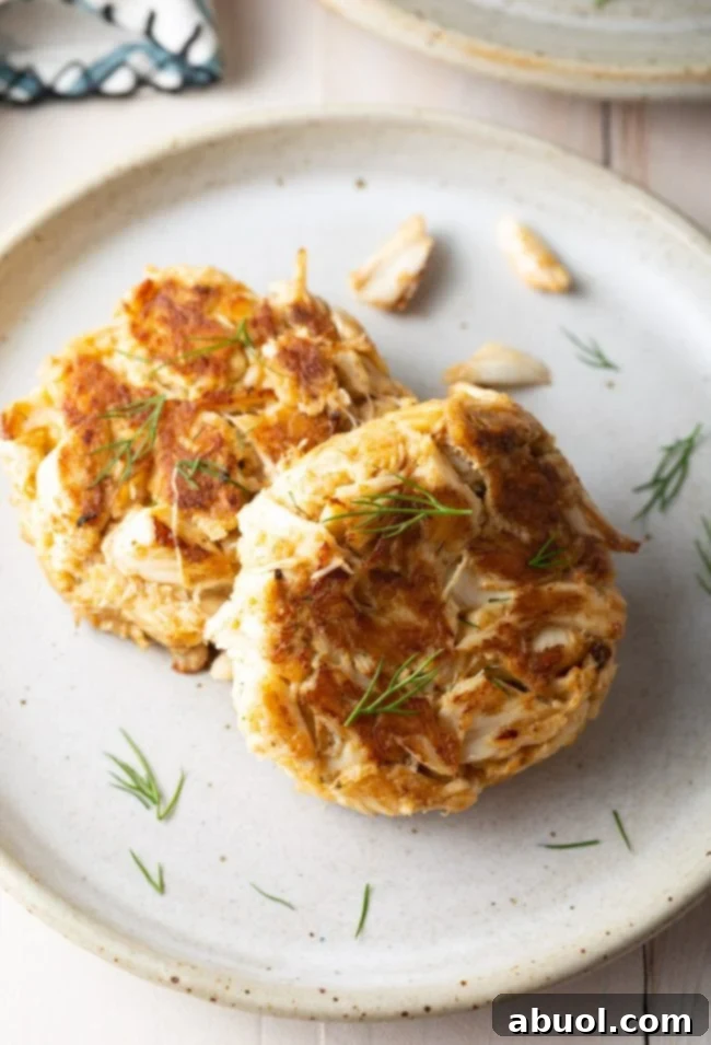 Two crab cakes plated with fresh dill as a garnish. 