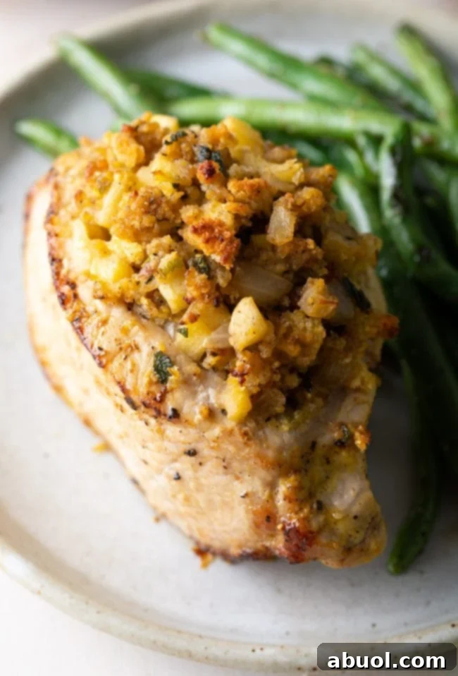 A close-up view of a baked apple stuffed pork chop, showcasing the golden exterior and the savory cornbread and apple filling, served with a side of green beans.