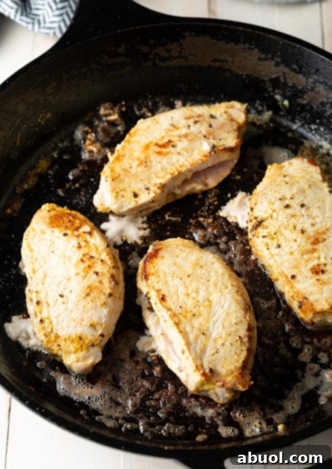 Top view of golden pan-seared pork chops in a cast iron skillet, showcasing their rich color before stuffing.