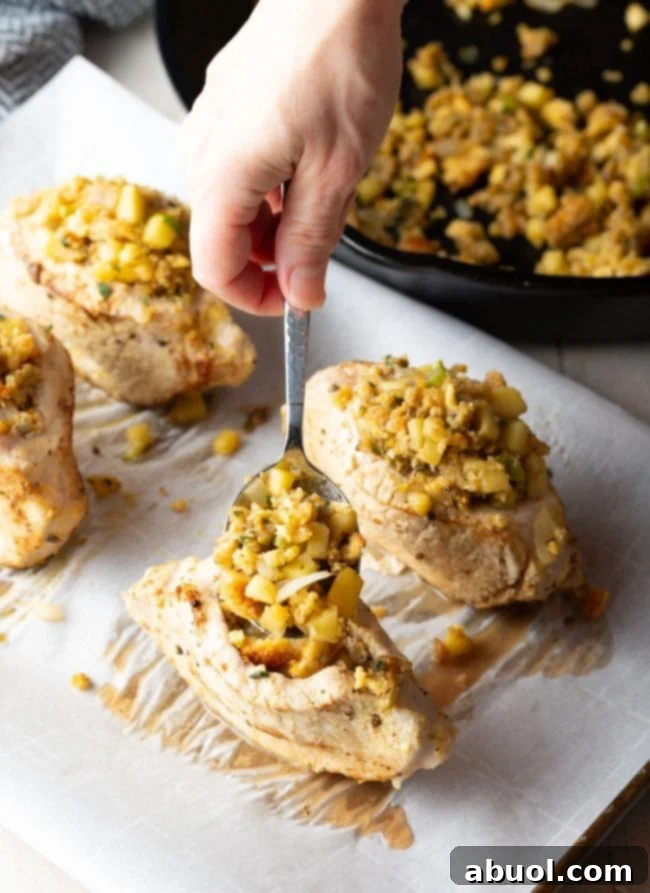 A beautifully plated stuffed pork chop, cut open to reveal the apple cornbread filling, next to a fresh green vegetable side.