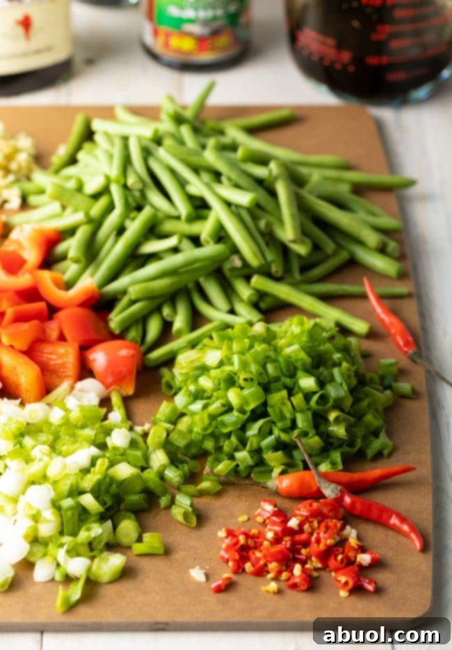 Freshly prepared ingredients for Thai basil chicken, including chopped green beans, red bell peppers, scallions, and fiery Thai bird chiles.