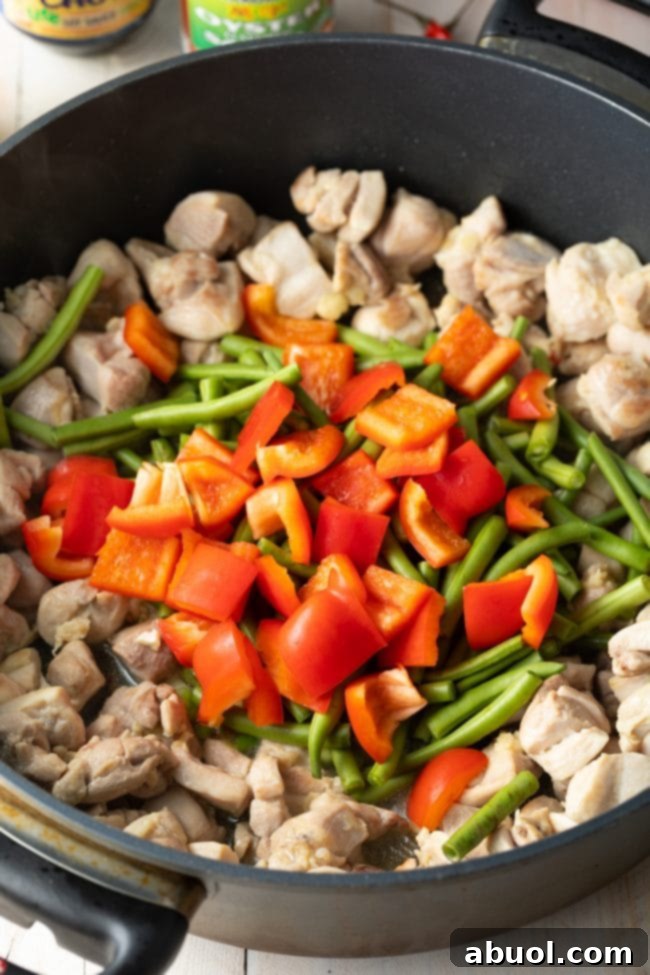 Chicken pieces and various vegetables being stir-fried in a hot skillet, showcasing the initial cooking process of Thai basil chicken.