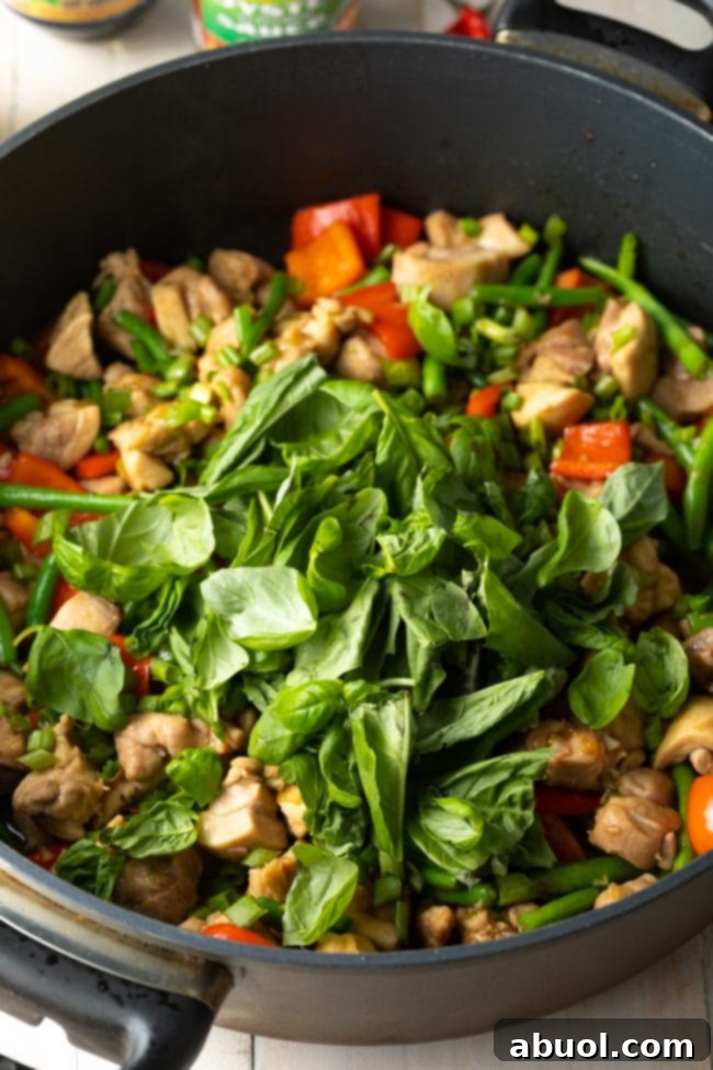 Fresh Thai basil leaves being added to the stir-fry in the pan, just before serving, to infuse the dish with its signature aroma.