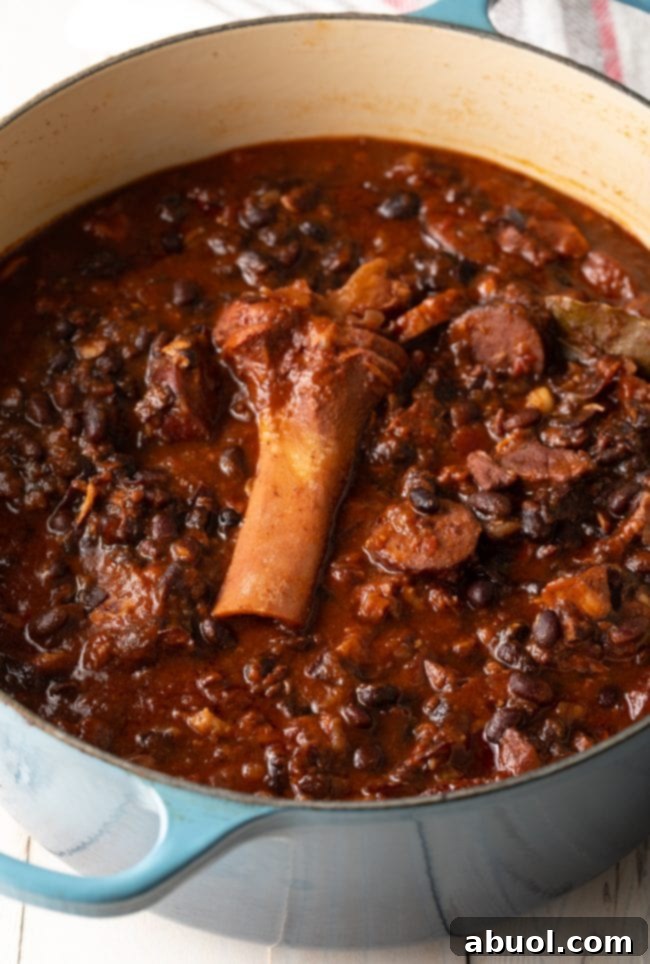 A large pot filled with the savory ingredients of Brazilian Feijoada, including various pork cuts, black beans, and tomatoes, actively simmering on the stovetop.