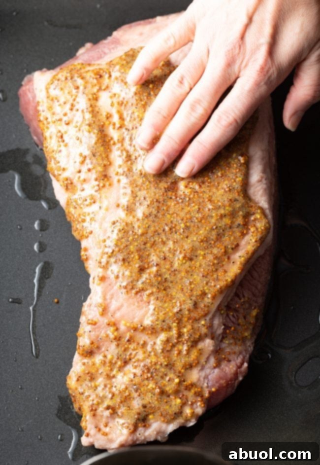 A hand seasoning corned beef brisket with a mustard and brown sugar mixture, creating a flavorful crust.