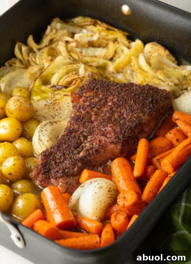 A perfectly roasted corned beef recipe, complete with tender cabbage and a vibrant mix of potatoes, carrots, and onions, served warm in a roasting pan.