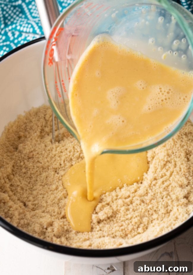 Wet ingredients, including whisked eggs, almond milk, and vanilla extract, being poured into the bowl of dry ingredients to form the pancake batter