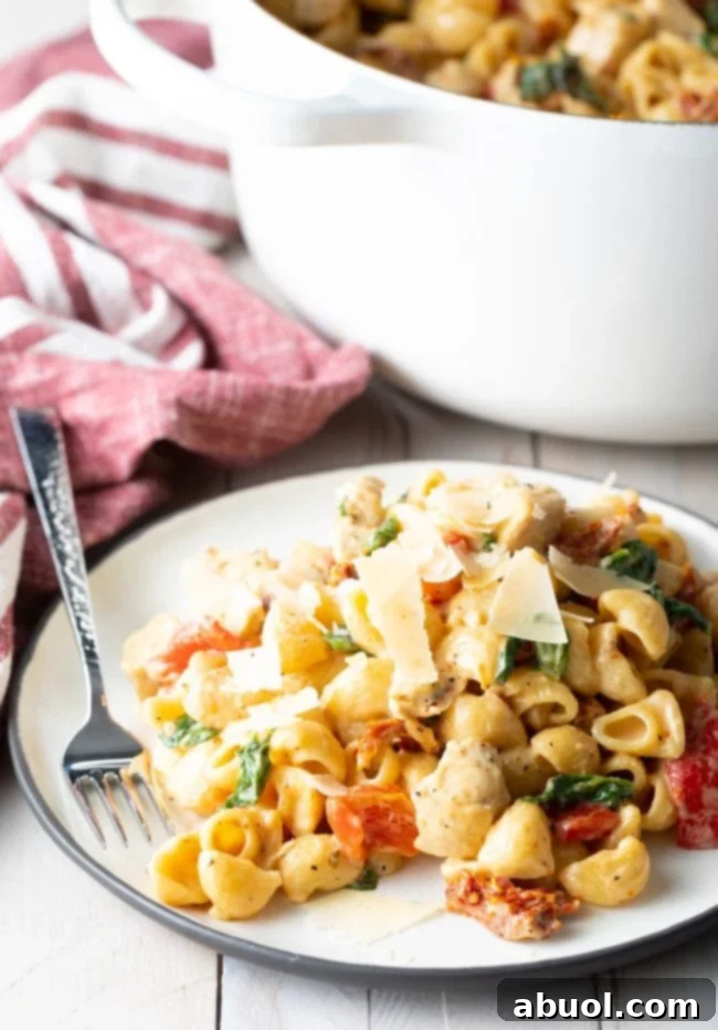 White plate of creamy tuscan chicken pasta with a fork on the side.