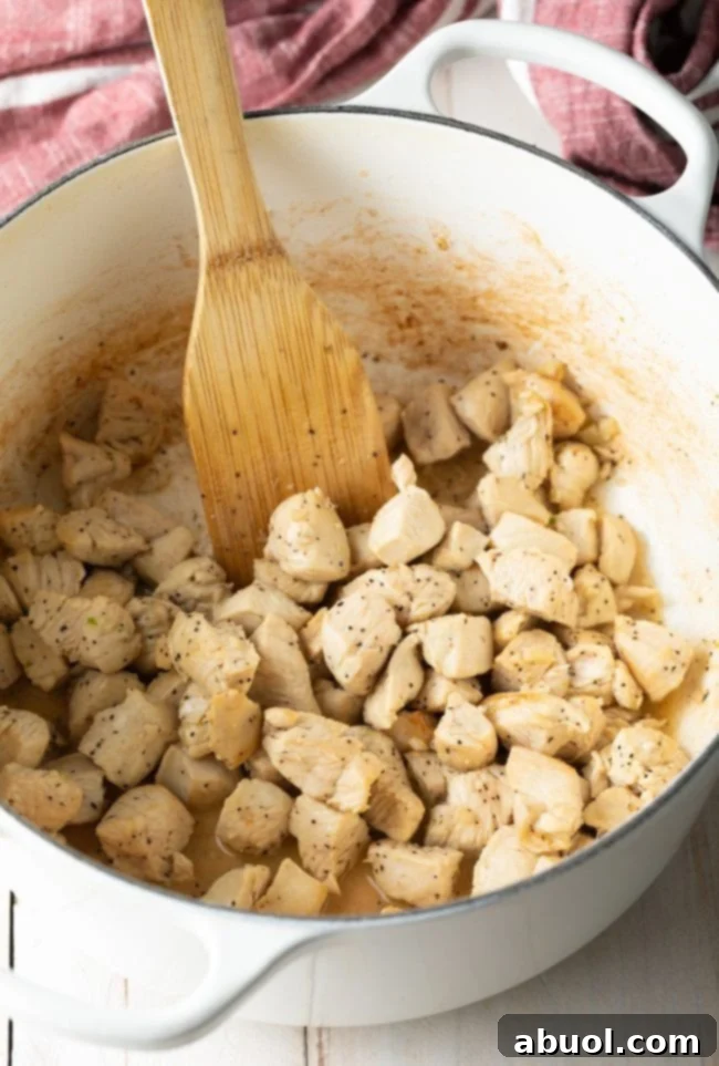 Sautéing chunks of chicken in a white dutch oven with a wood spatula.