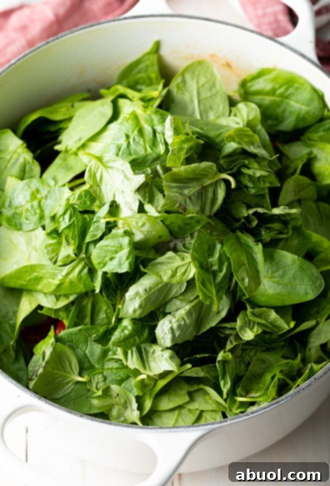 Spinach added to the white pot of tuscan chicken pasta.