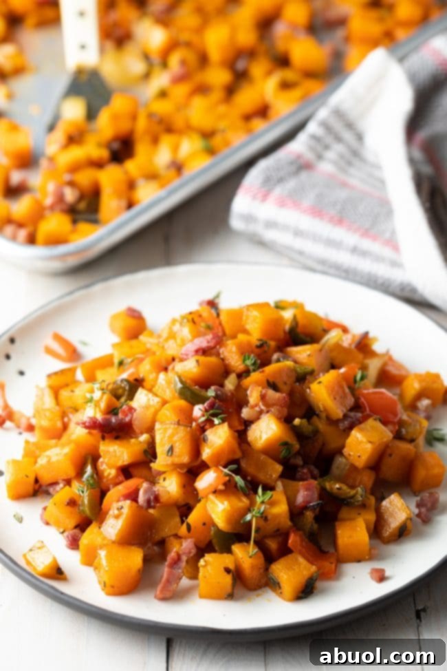 Sweet potato hash browns on a white plate with a baking sheet in the background, showcasing its golden crispiness.