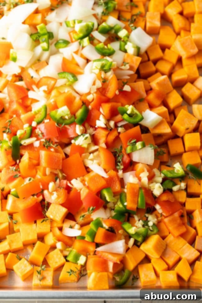 Chopped sweet potatoes, bell peppers, onions, and jalapeños spread on a baking sheet, ready for roasting.