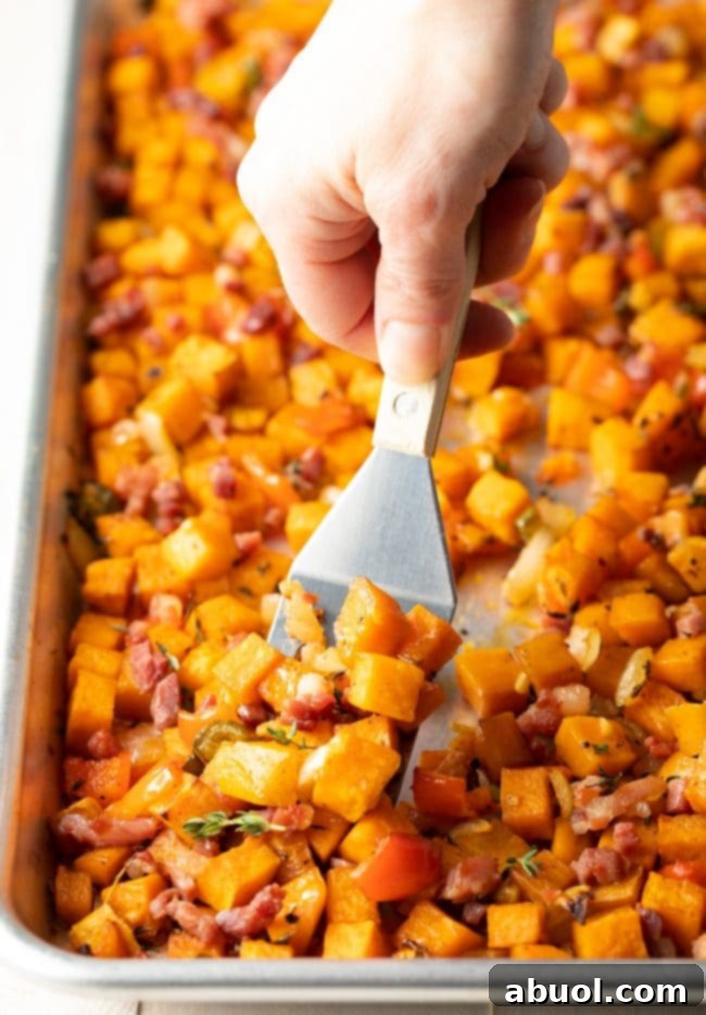 A spatula flipping the roasting sweet potato hash on a baking sheet to ensure even browning.