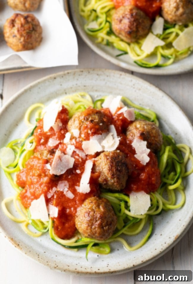 Plate of healthy baked turkey meatballs served alongside fresh zucchini noodles, garnished with herbs.