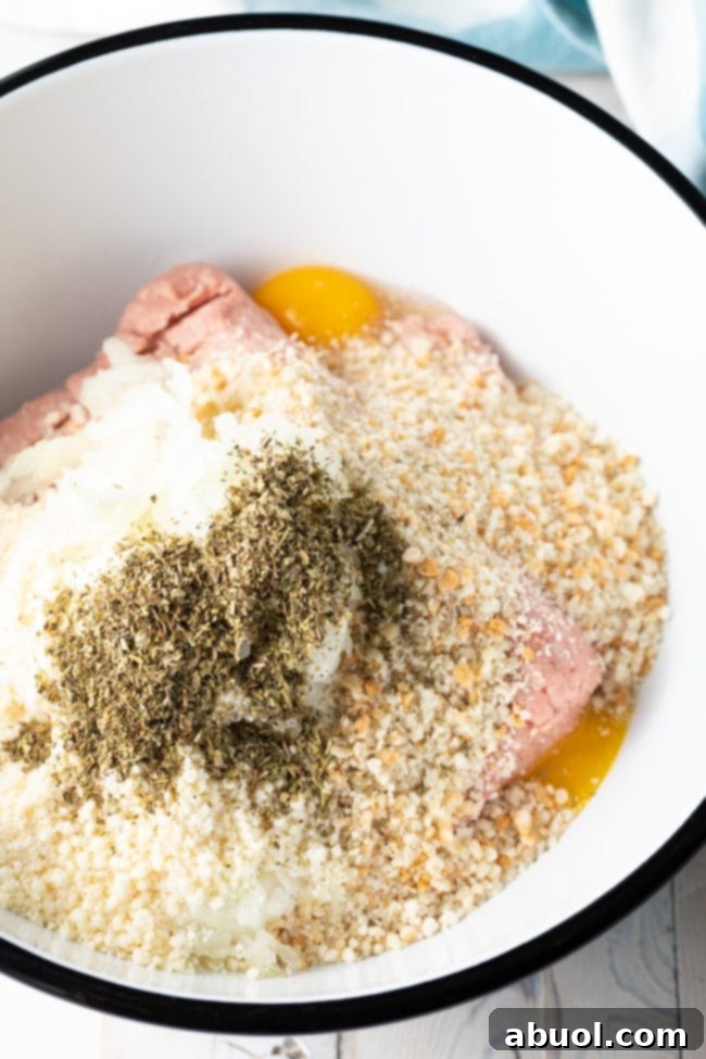 All raw ingredients for turkey meatballs, including ground turkey, panko, cheese, onion, eggs, and spices, mixed in a large bowl.