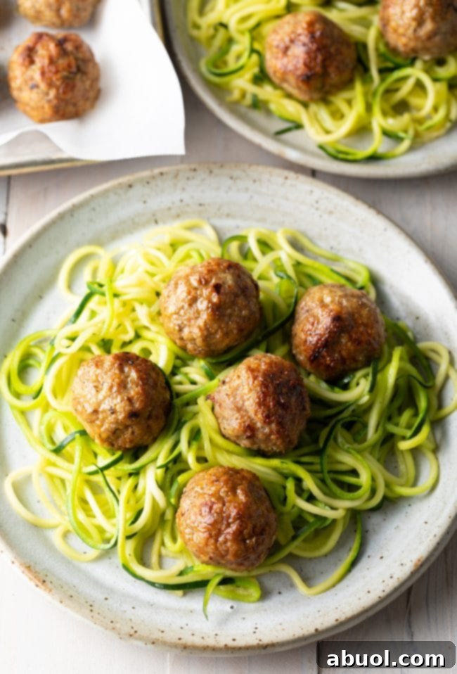 Healthy low-carb turkey meatballs served simply with spiralized zucchini noodles (zoodles) on a white plate, no sauce.