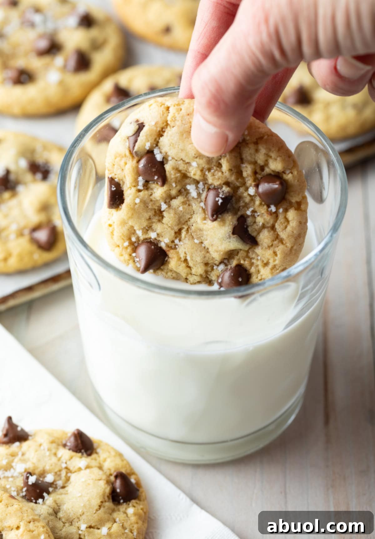Salted Chocolate Chunk Delights 11 Hand dunking a salted chocolate chip cookie into a glass of milk.