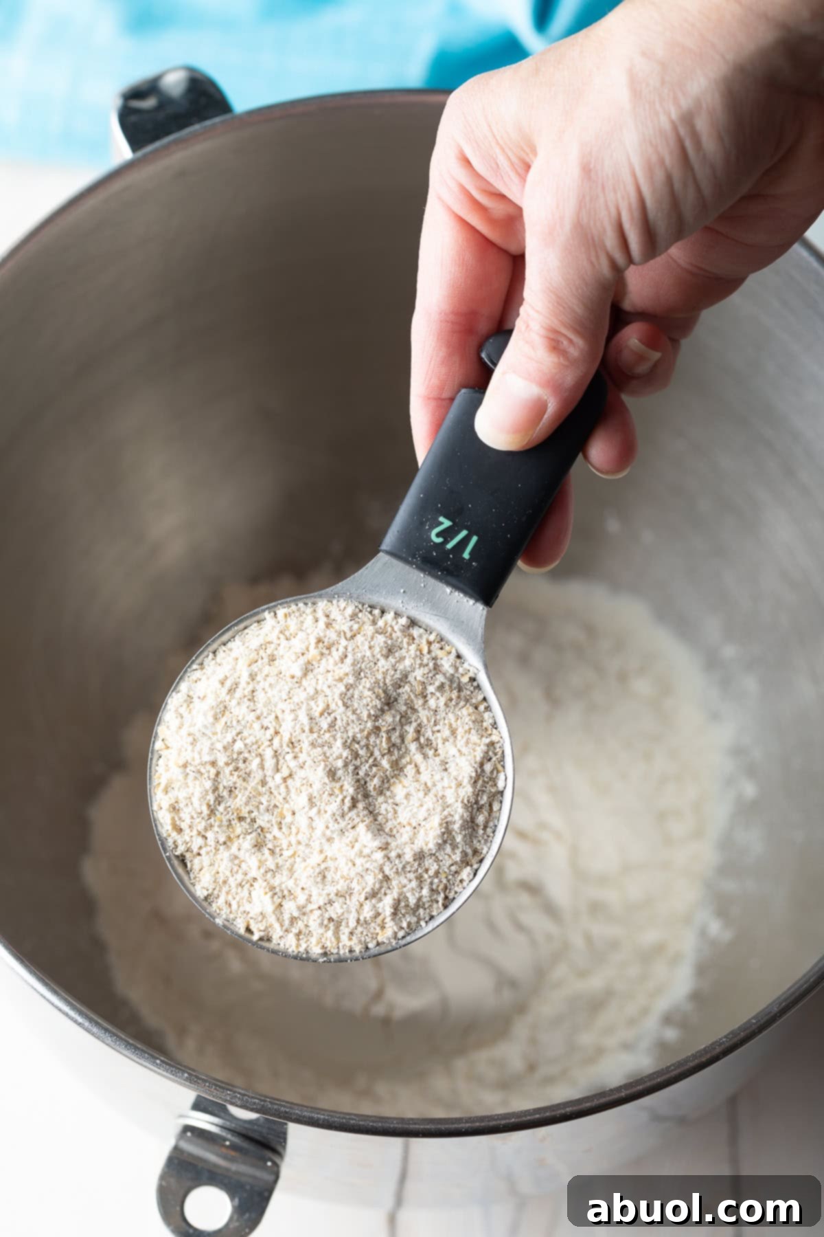 Salted Chocolate Chunk Delights 6 Hand adding oat flour to a metal mixing bowl containing other dry ingredients.