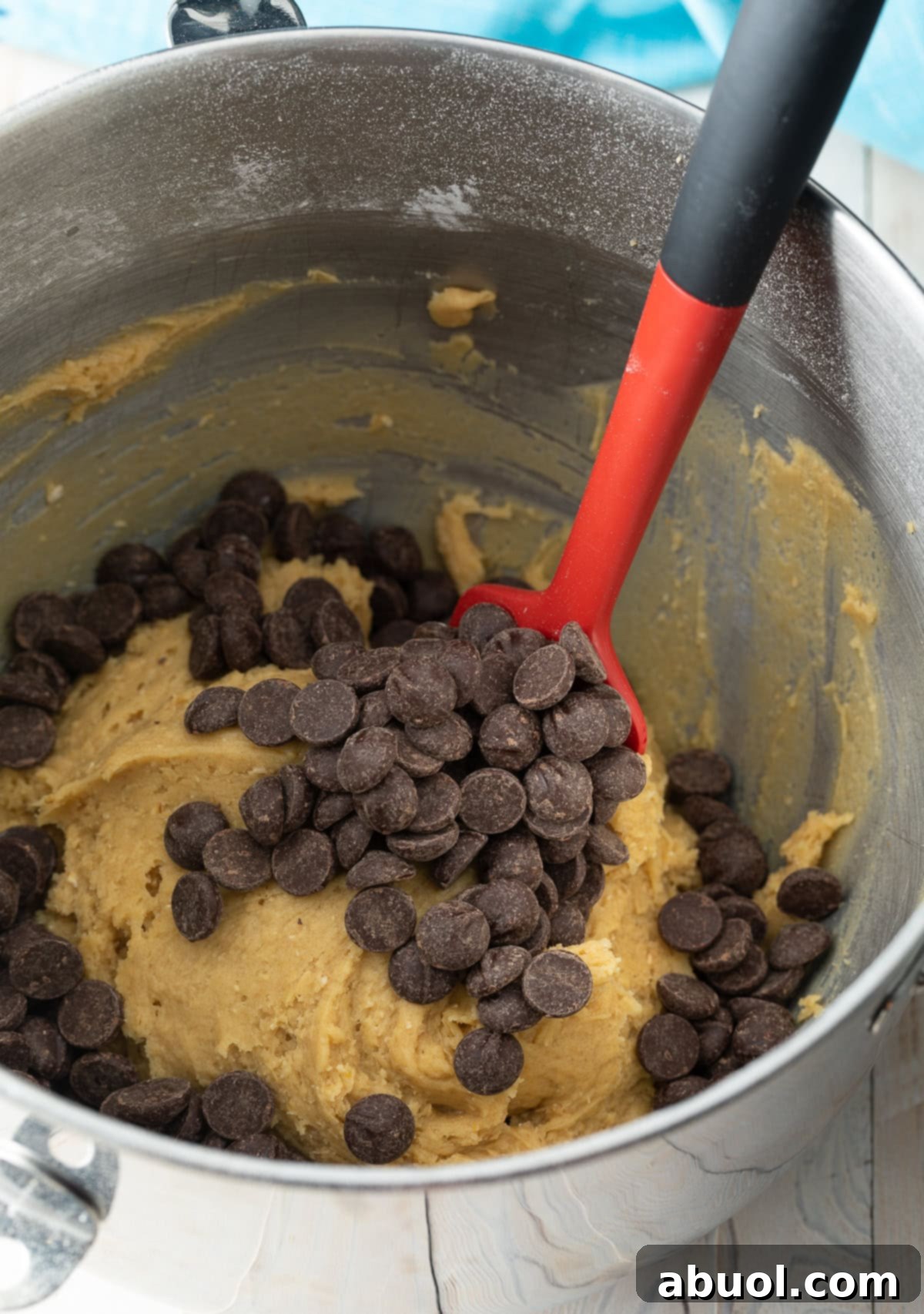 Salted Chocolate Chunk Delights 8 Using a red spatula to stir chocolate chips into cookie dough in a metal mixing bowl.
