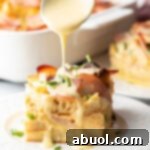 Slice of eggs benedict casserole with hollandaise being drizzled over it with a spoon.