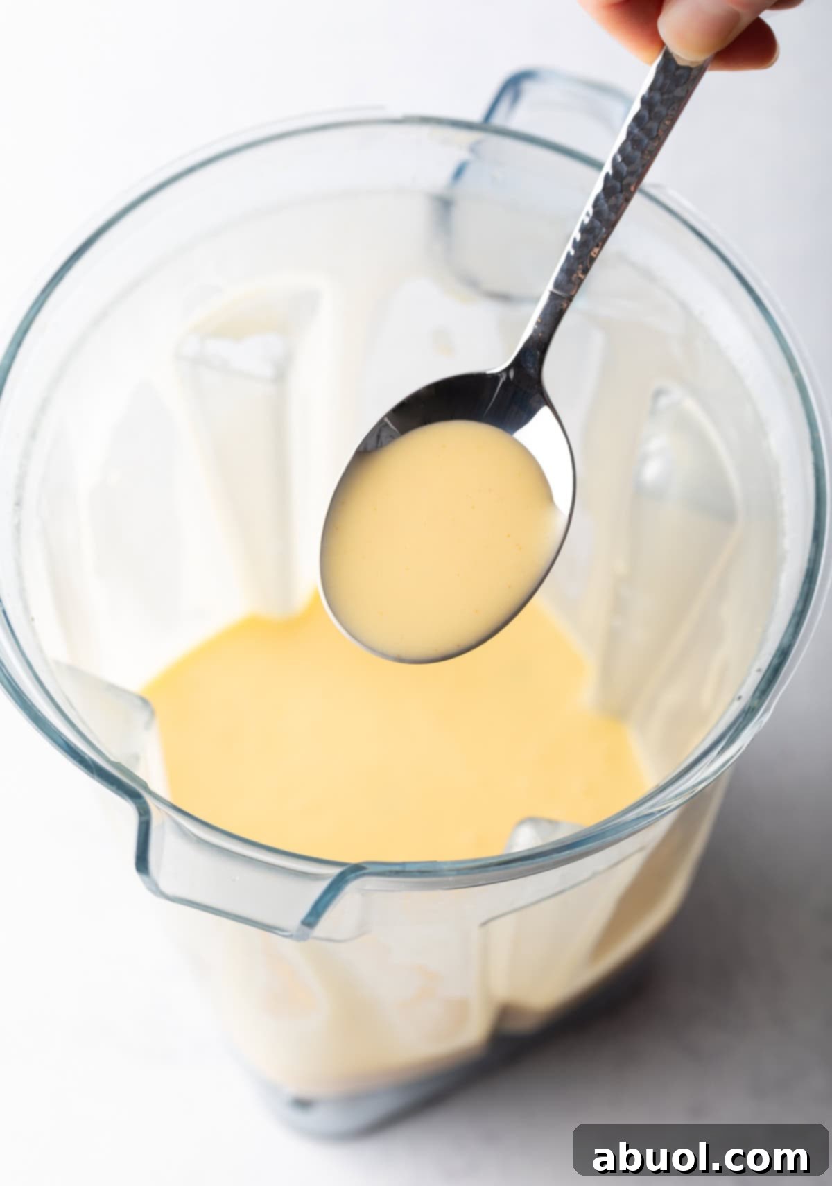 Spoon holding Hollandaise sauce over a blender