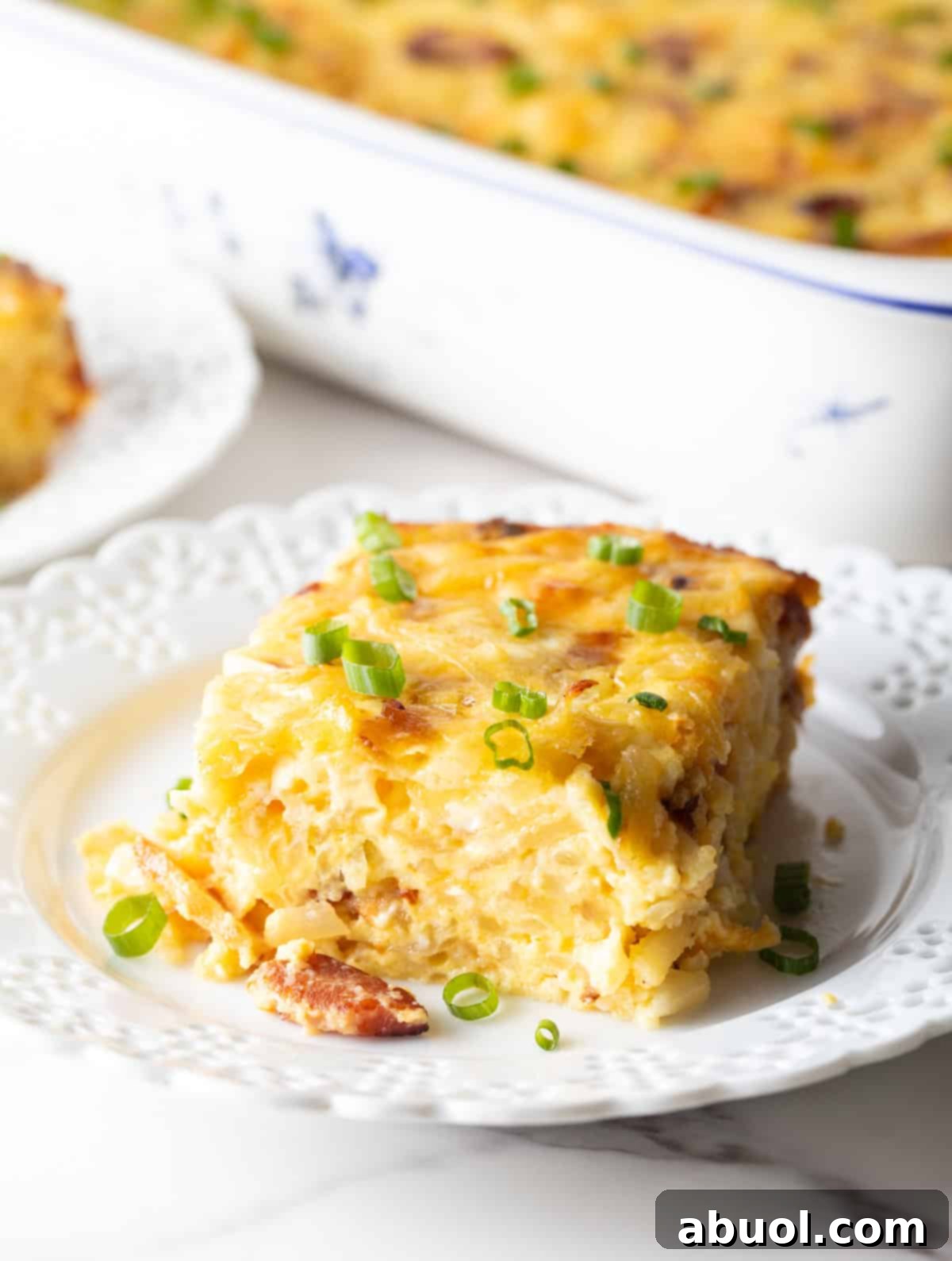 Amish Breakfast Casserole: A square serving of hash brown potato, egg and cheese casserole on a white plate.