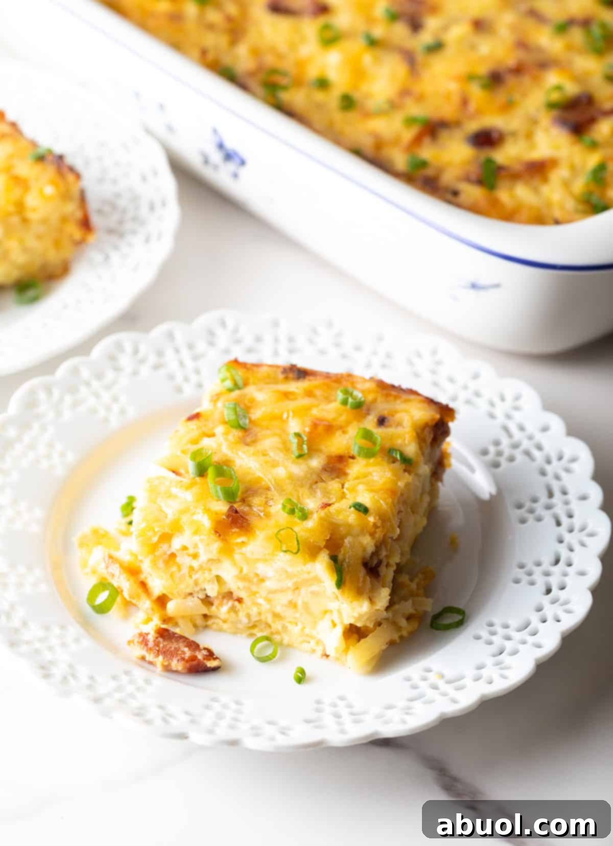 Amish Breakfast Casserole: Square serving of hash brown potato, egg and cheese casserole on a white plate.
