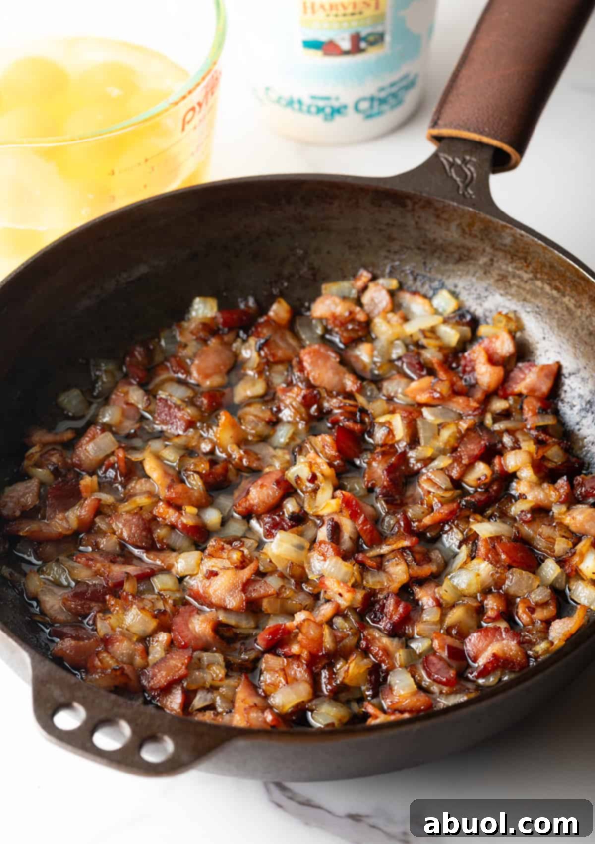 Amish Breakfast Casserole: Cooking chopped bacon and onions in a cast iron skillet.