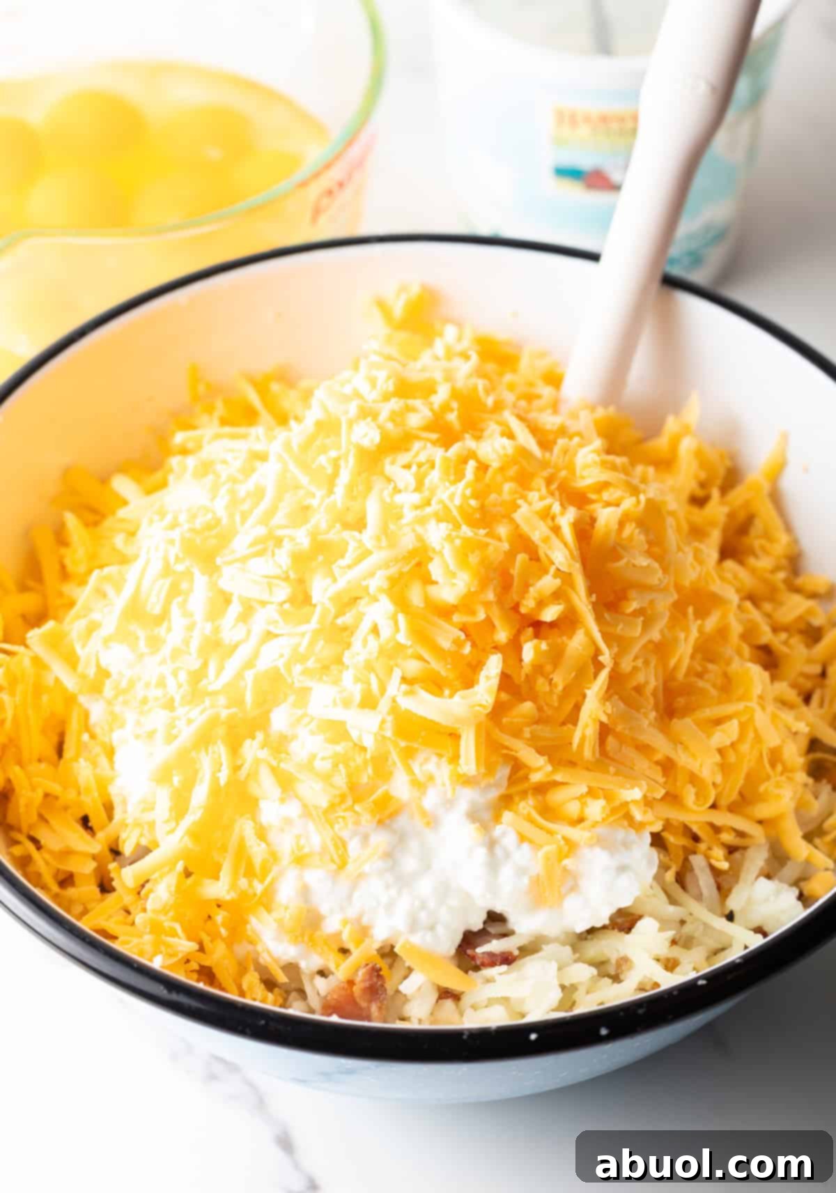 Amish Breakfast Casserole: Adding shredded cheese to a bowl with cottage cheese, shredded potatoes and bacon.