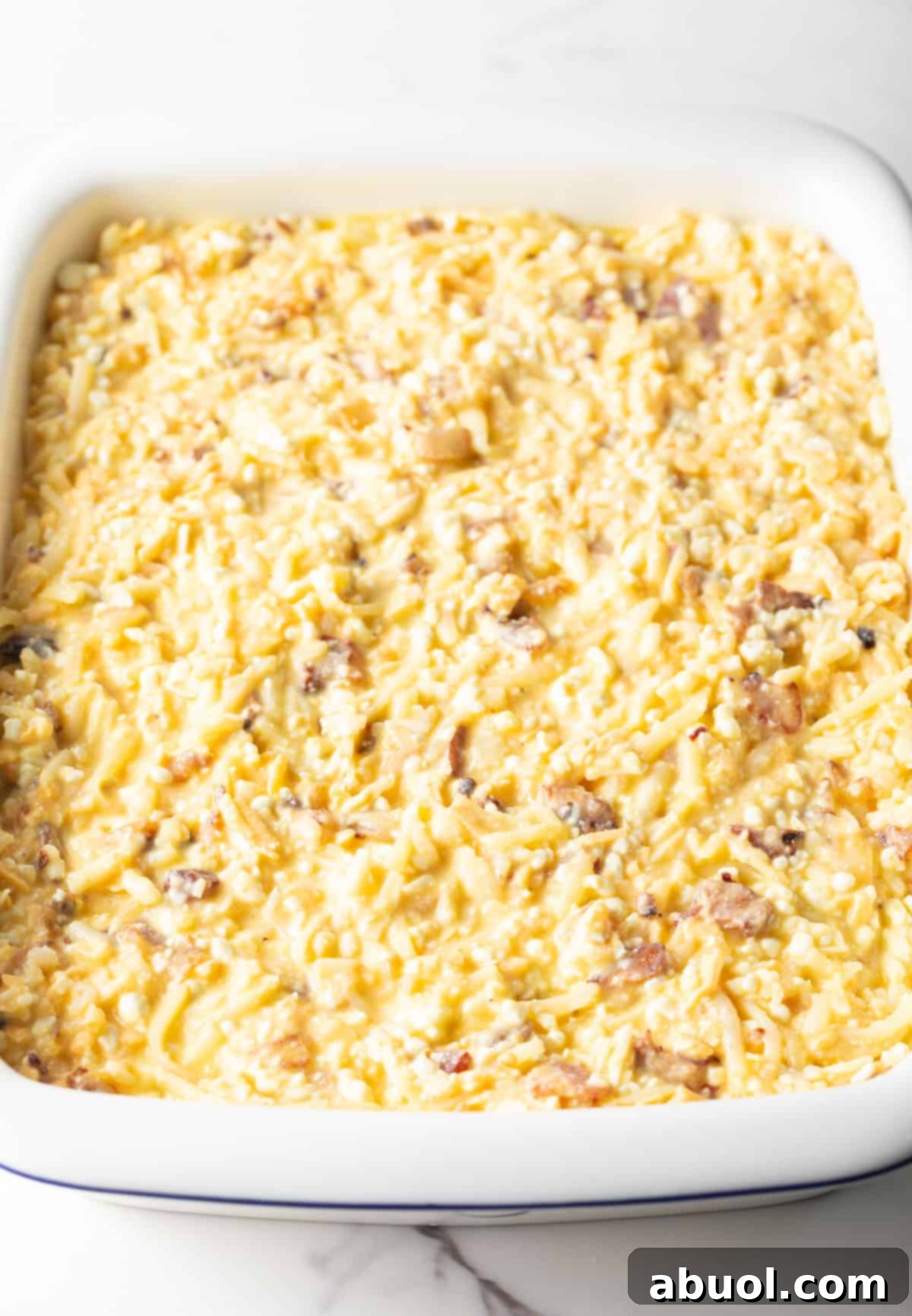 Amish Breakfast Casserole: Shredded hashbrown potatoes with cheese, bacon and eggs in a white baking dish.
