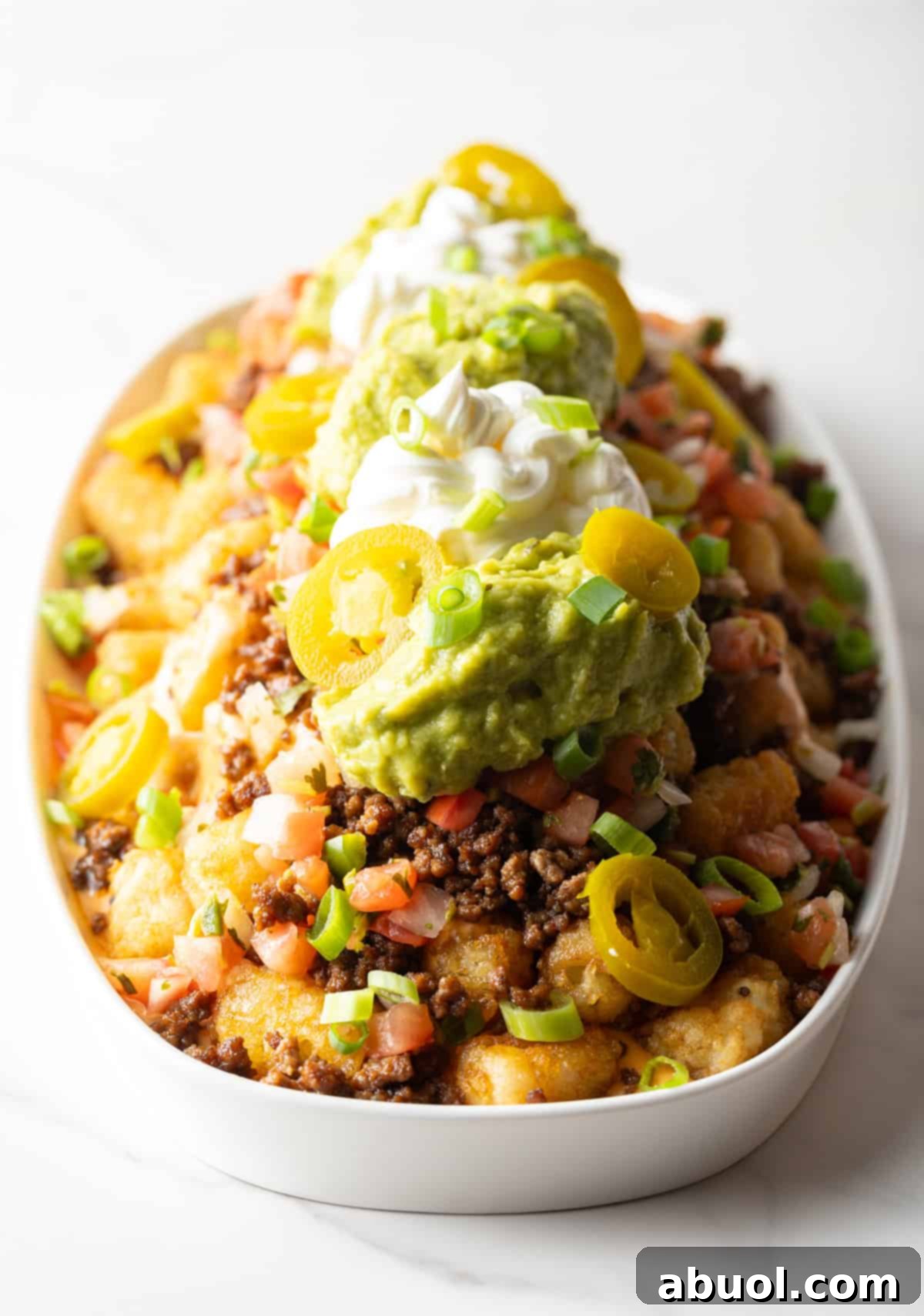 Large serving dish of loaded tater tots with ground beef, jalapenos, salsa, cheese, guacamole, and sour cream