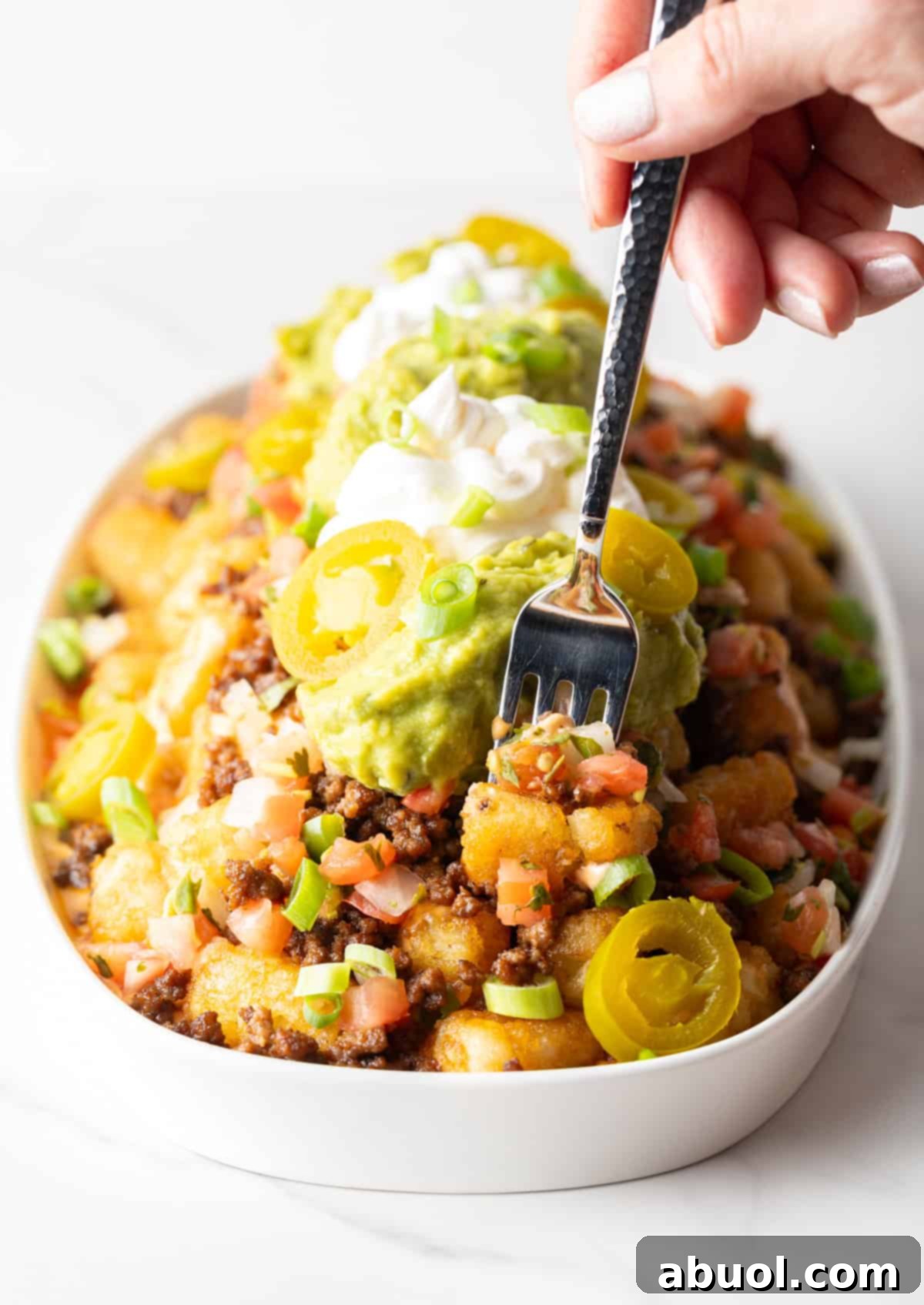 Hand holding a fork with loaded tater tots