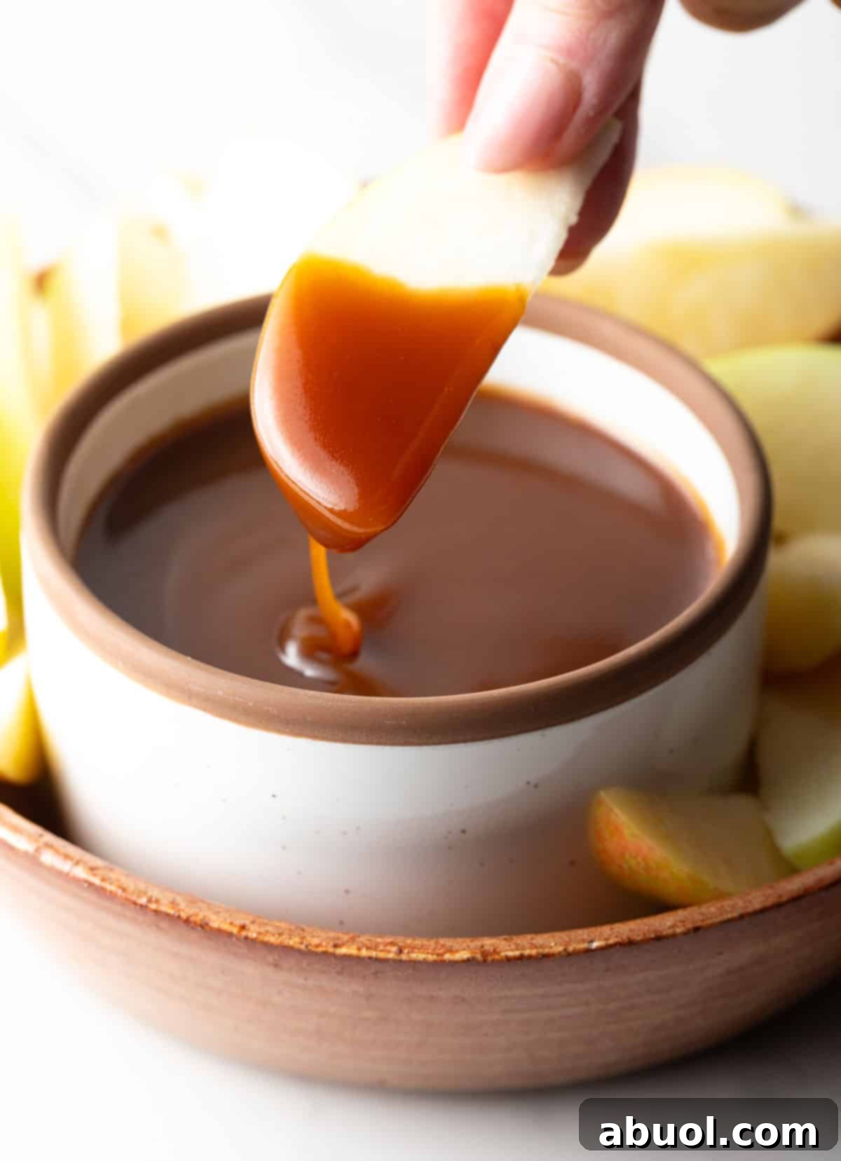 An apple slice being dipped into salted caramel sauce