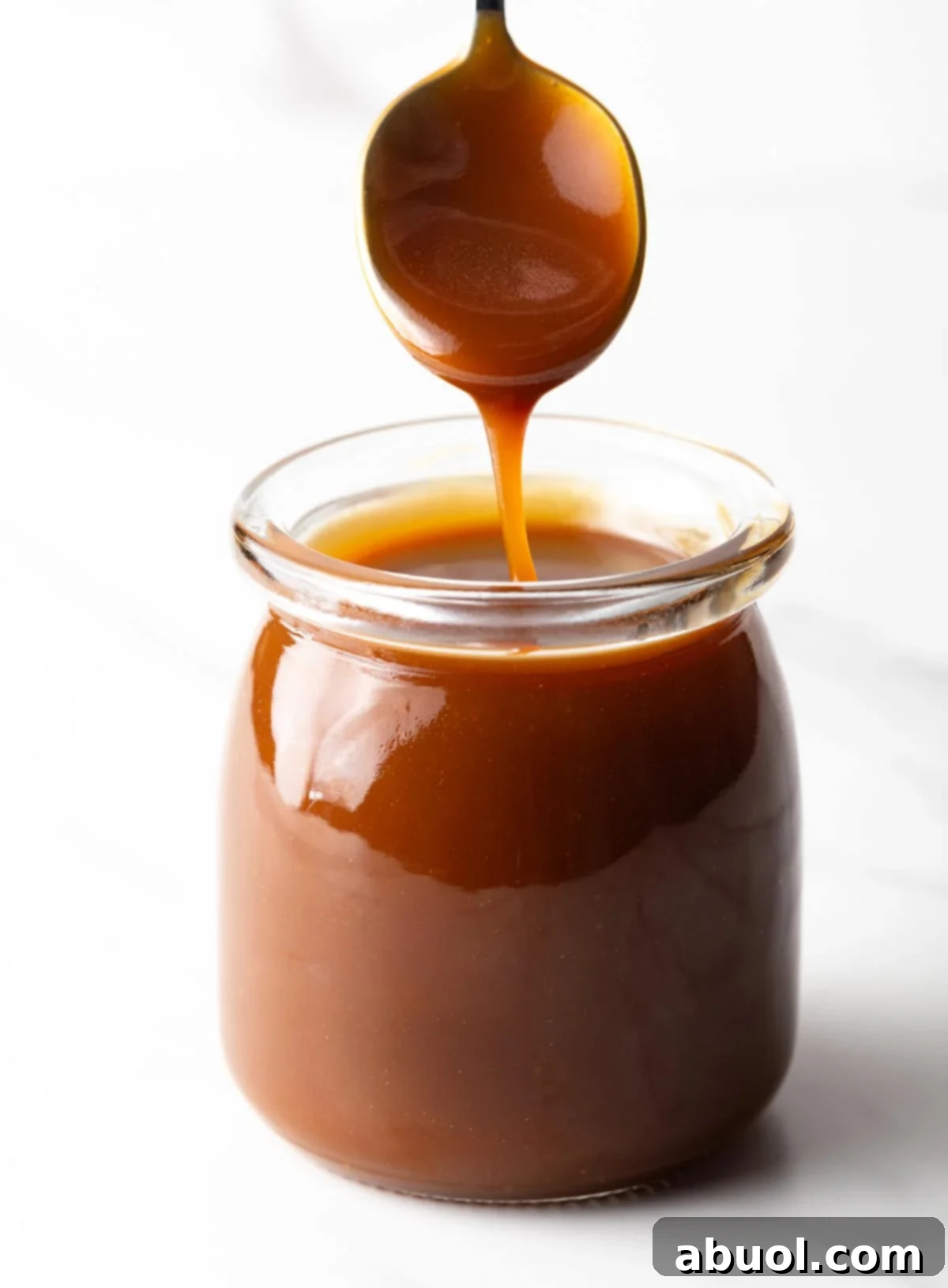 Homemade salted caramel sauce being drizzled into a glass jar