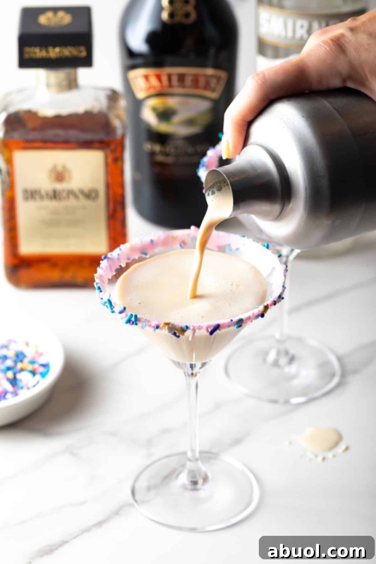 Creamy sugar cookie cocktail with a colorful rim, surrounded by liquor bottles, emphasizing the richness and deliciousness of the Sugar Cookie Martini.