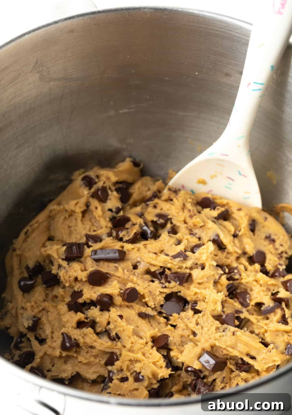 Using a spatula to stir chocolate chunks into brown sugar cookie dough.