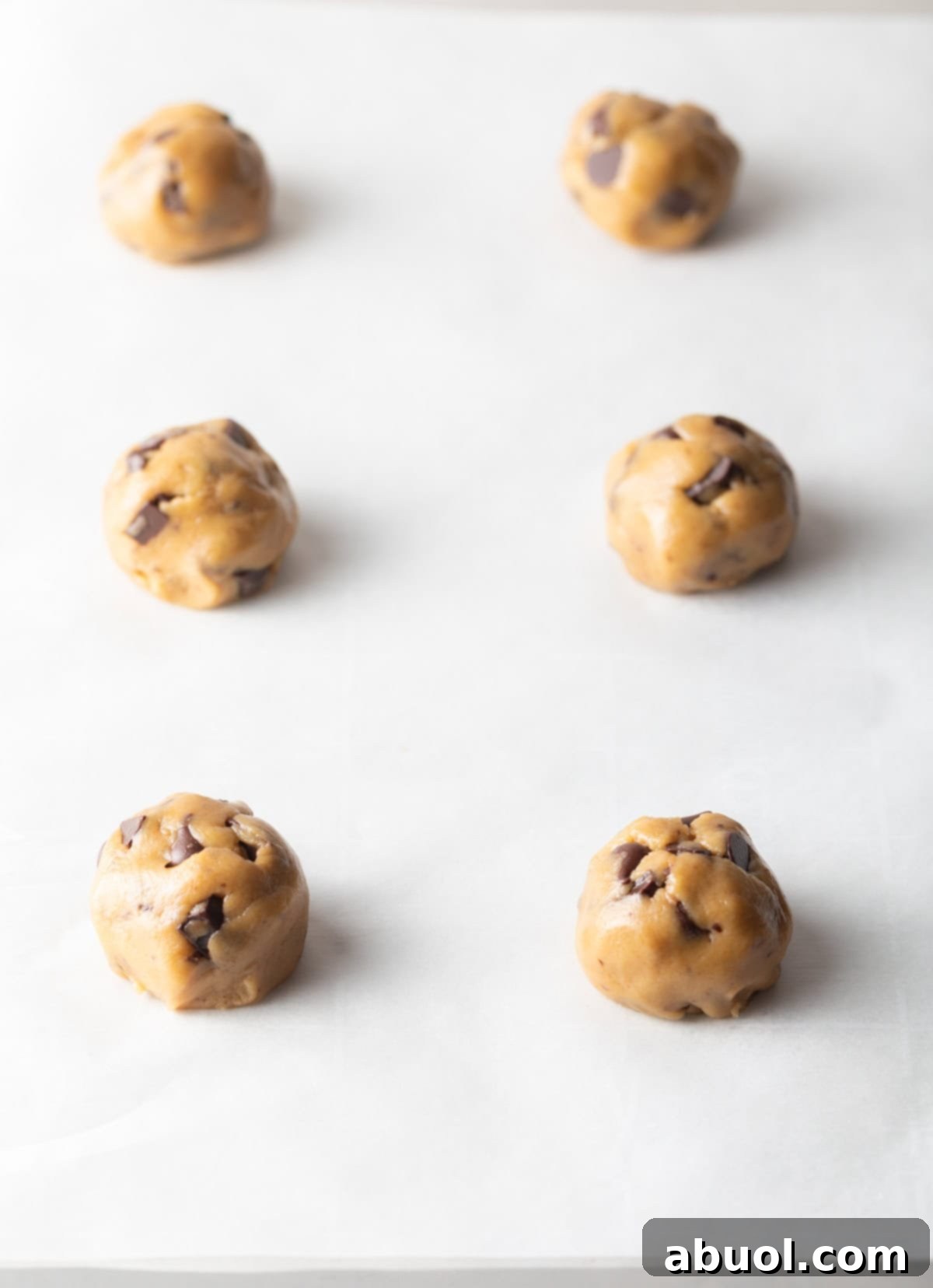 Six balls of brown sugar chocolate chip cookie dough on a baking sheet.