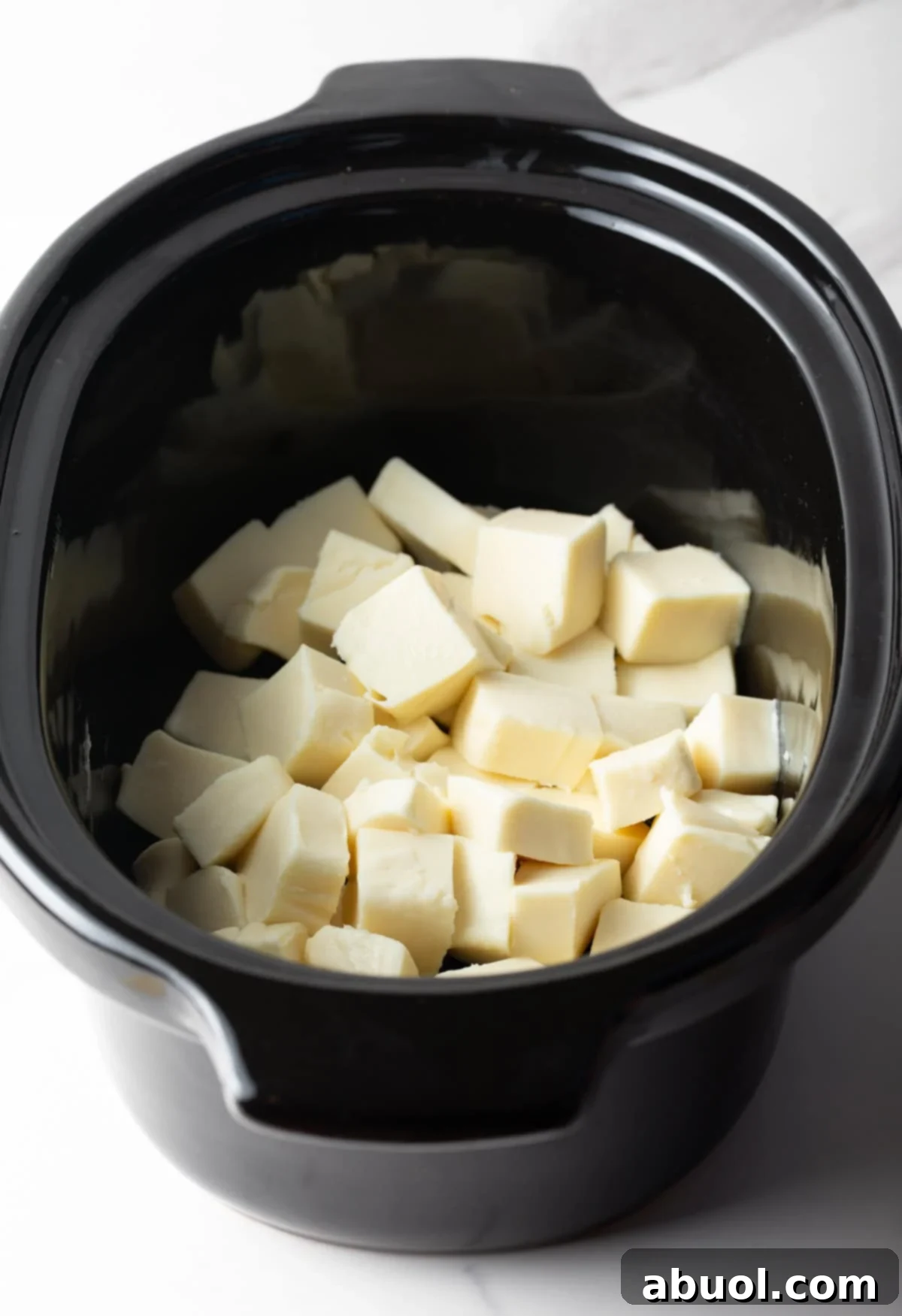 Cubed white American cheese sitting in a black crock pot.