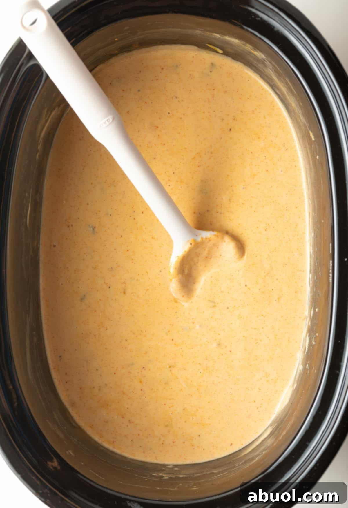 Black slow cooker filled with queso dip with a white spoon stirring it.