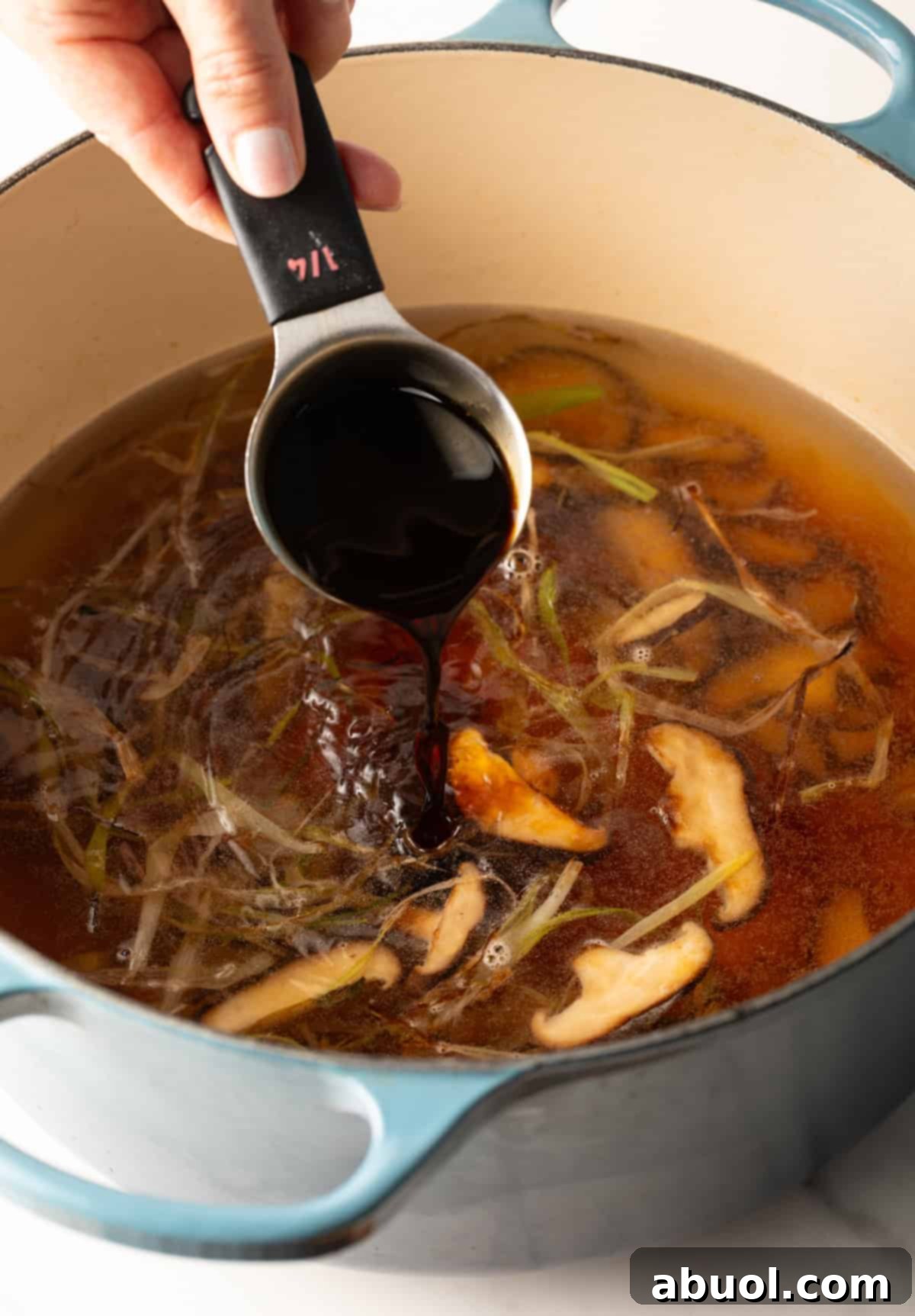 A measuring cup adding soy sauce to udon noodle soup broth.