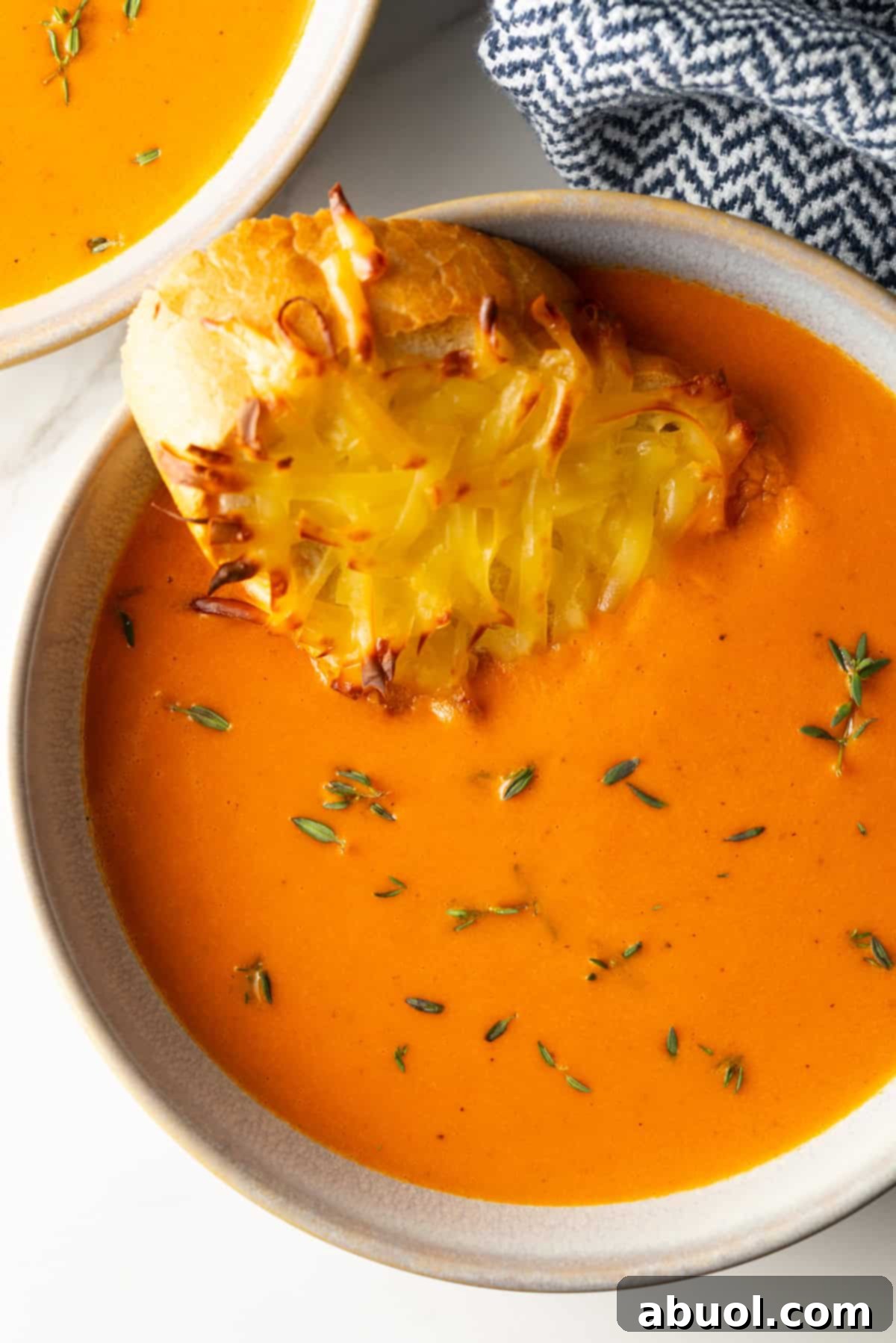 Bowl of red pepper gouda soup with cheesy baguette slice