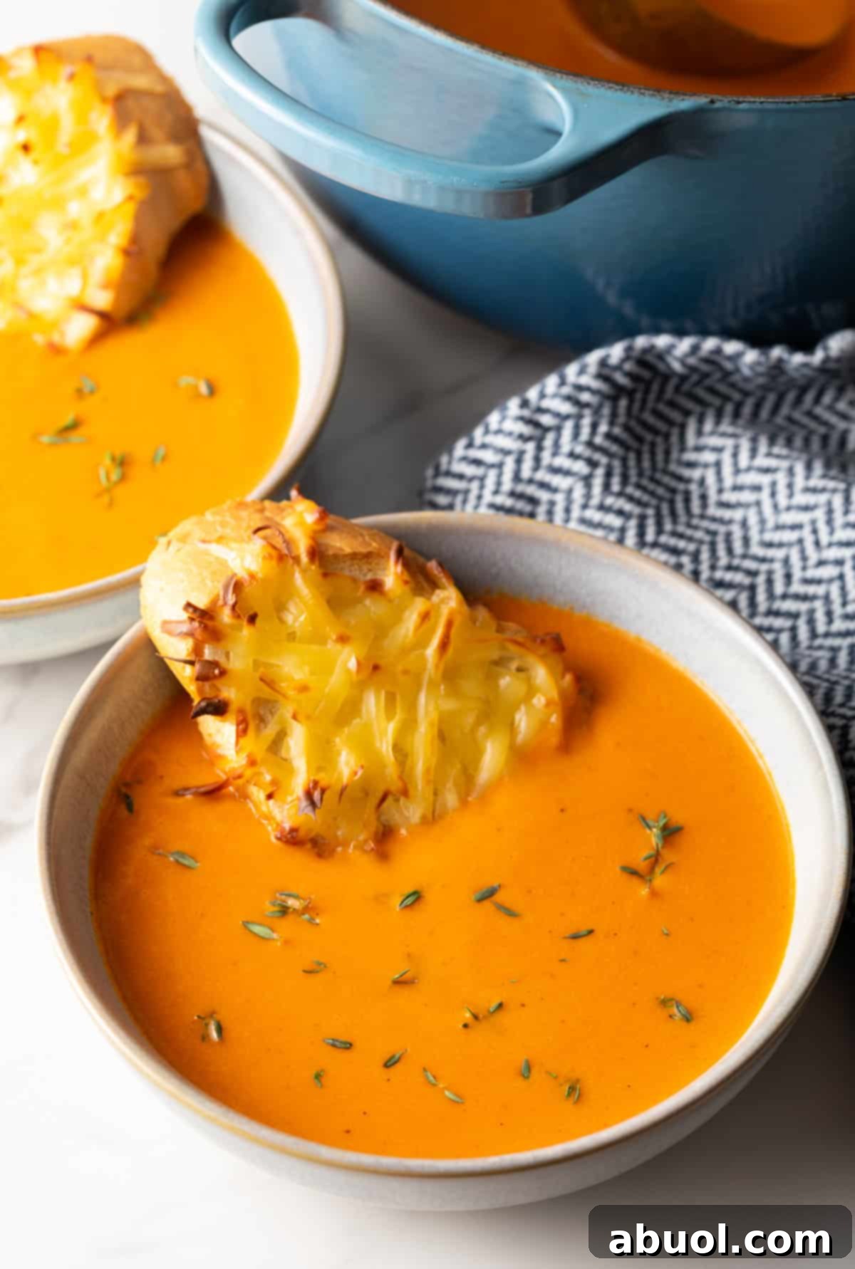 A bowl of red pepper gouda soup with cheesy baguette slice