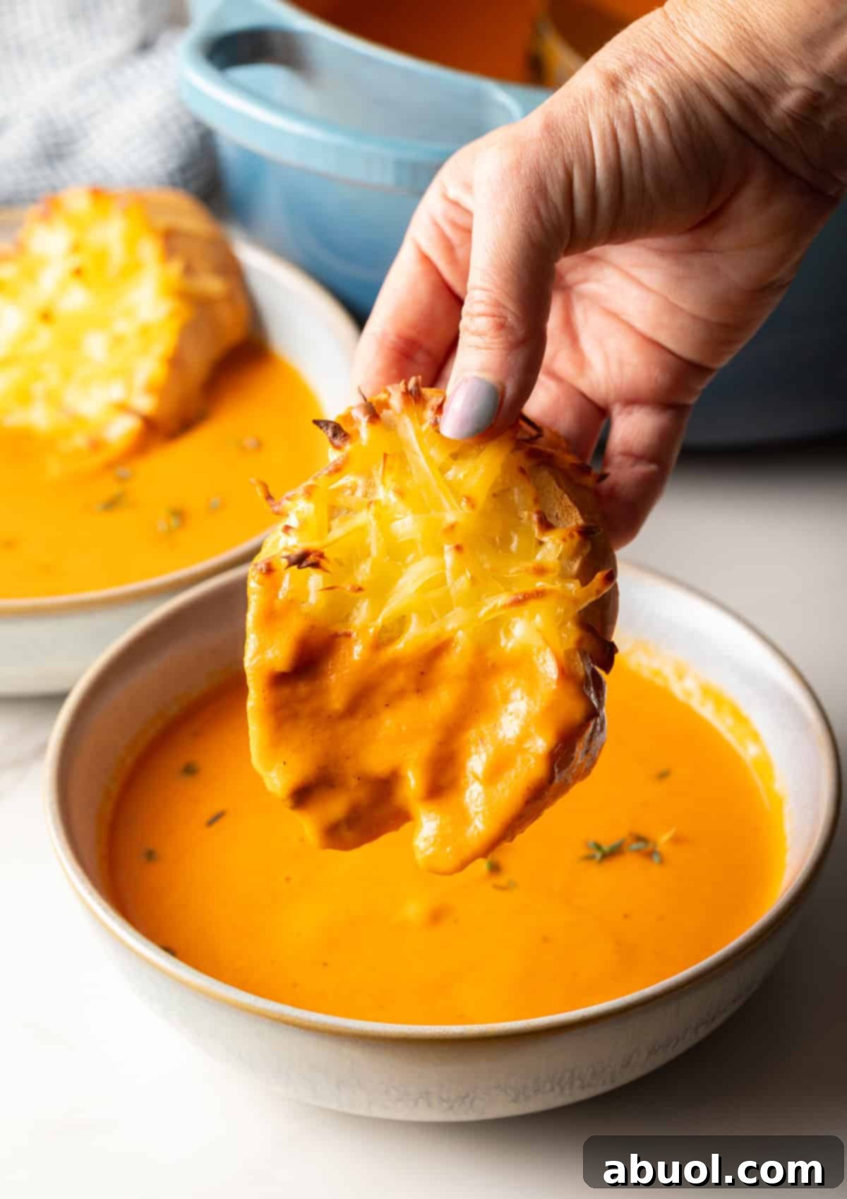 Dipping cheesy bread into a bowl of red pepper gouda soup