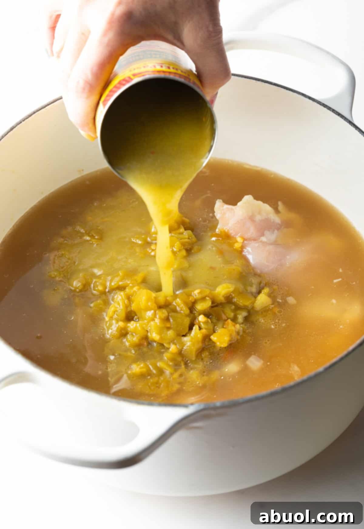 Pouring verde enchilada sauce from a can into a simmering pot of soup.