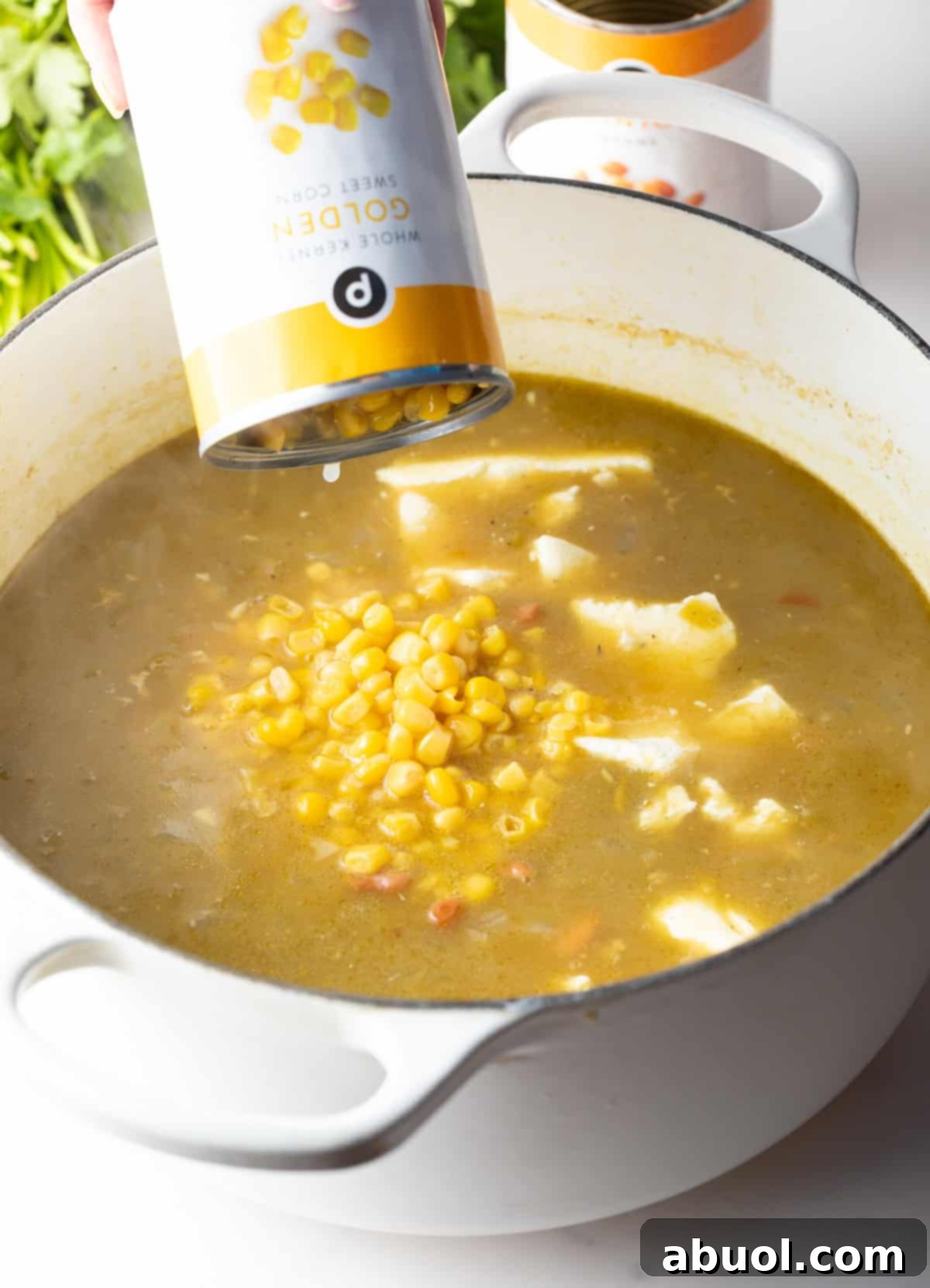 Pouring canned corn into a large pot of chicken soup.