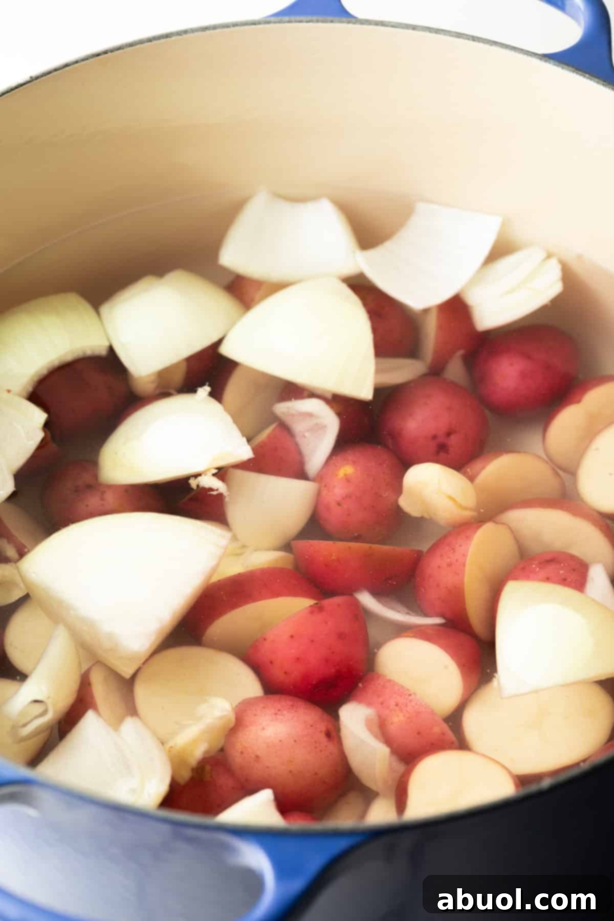 A pot filled with water, onion wedges, and baby red potatoes.
