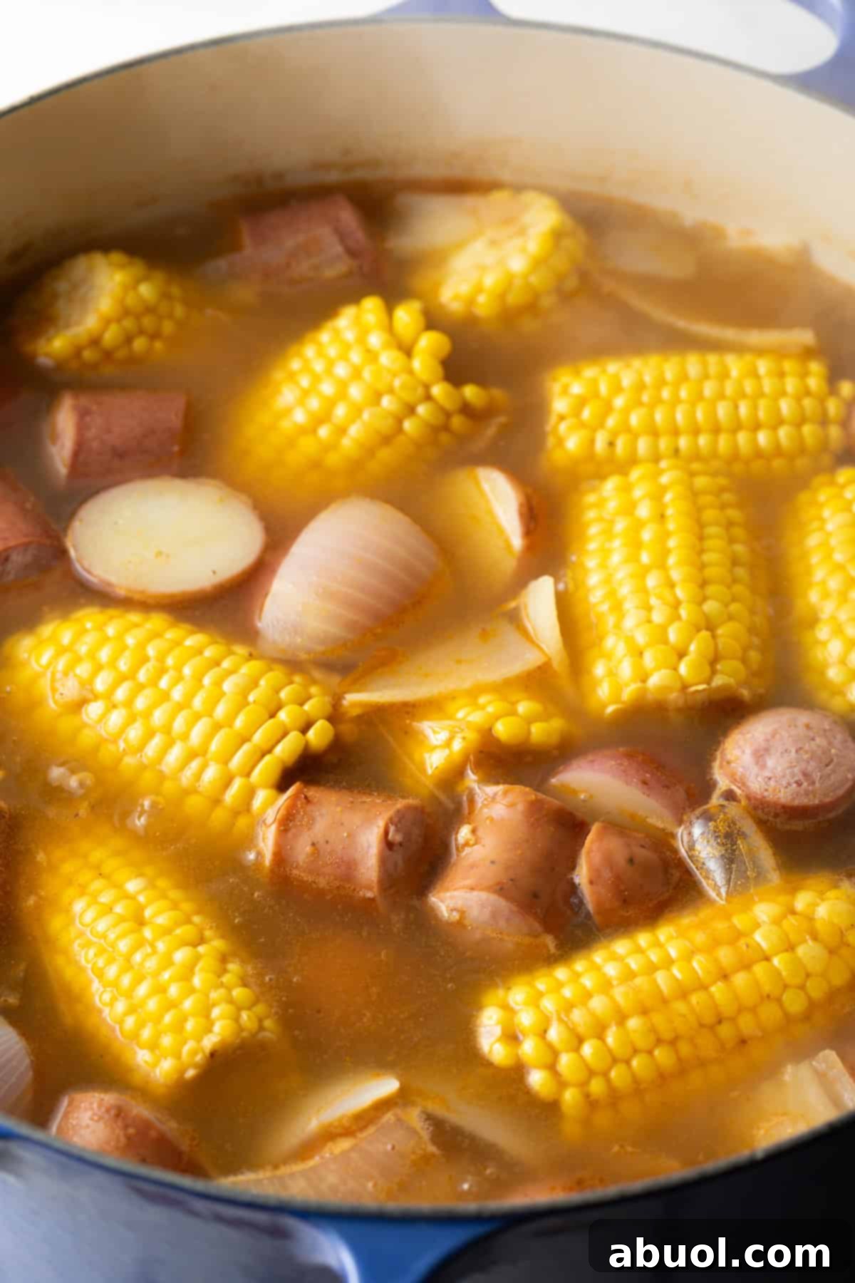 A pot of Old Bay seasoning spiced broth with corn, potatoes, onions, and sausage.