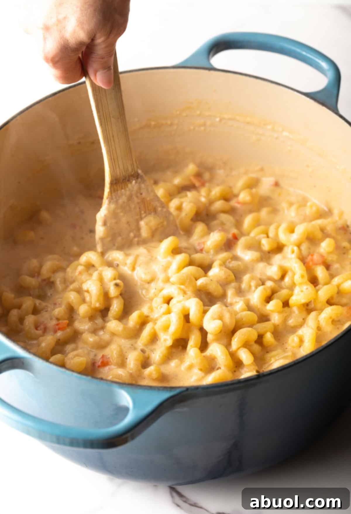 A wooden spoon stirring pasta into cheese sauce