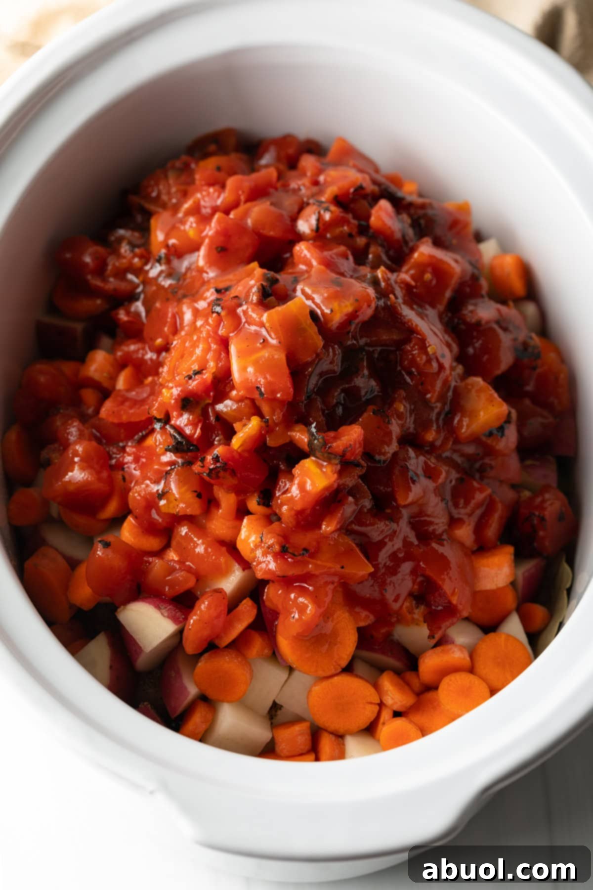 Savory Slow Cooker Chicken Stew 8 Canned diced tomatoes added to the vegetables in a white slow cooker.