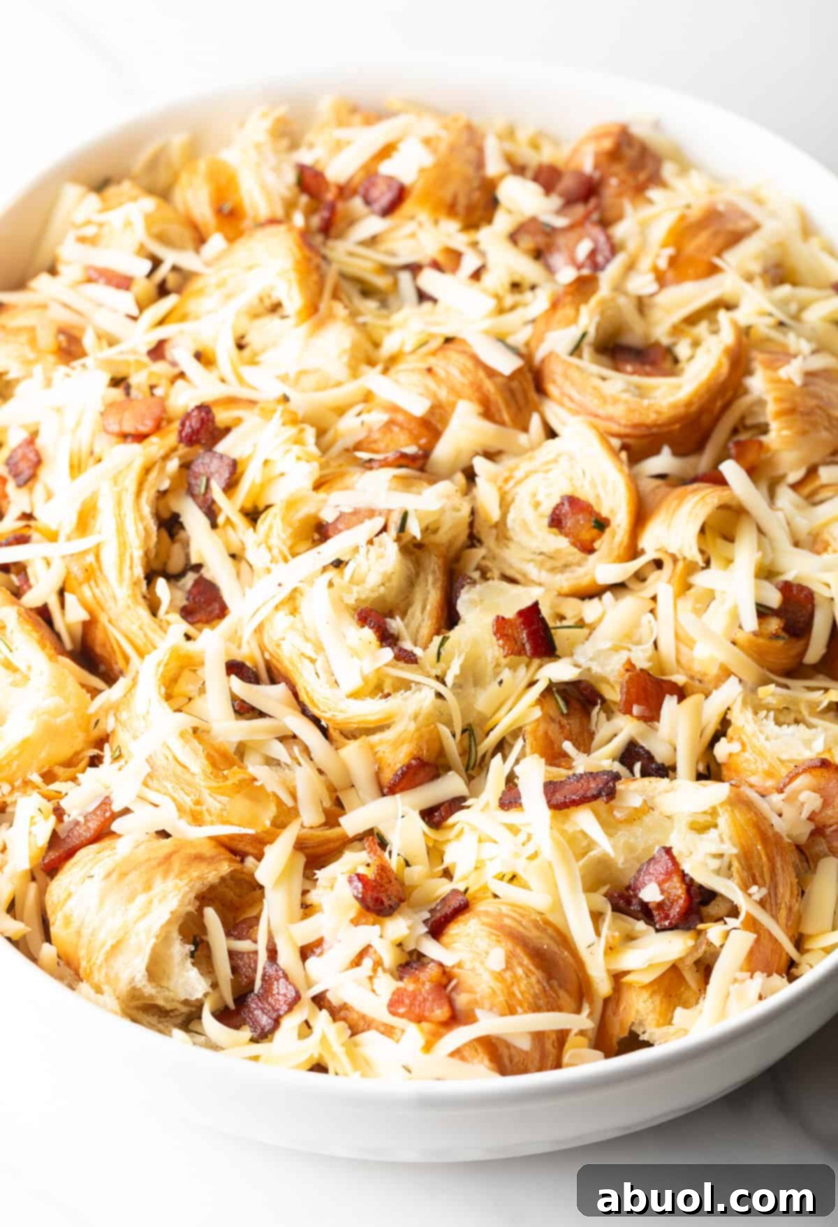 Shredded cheese is mixed into the unbaked croissant breakfast casserole.